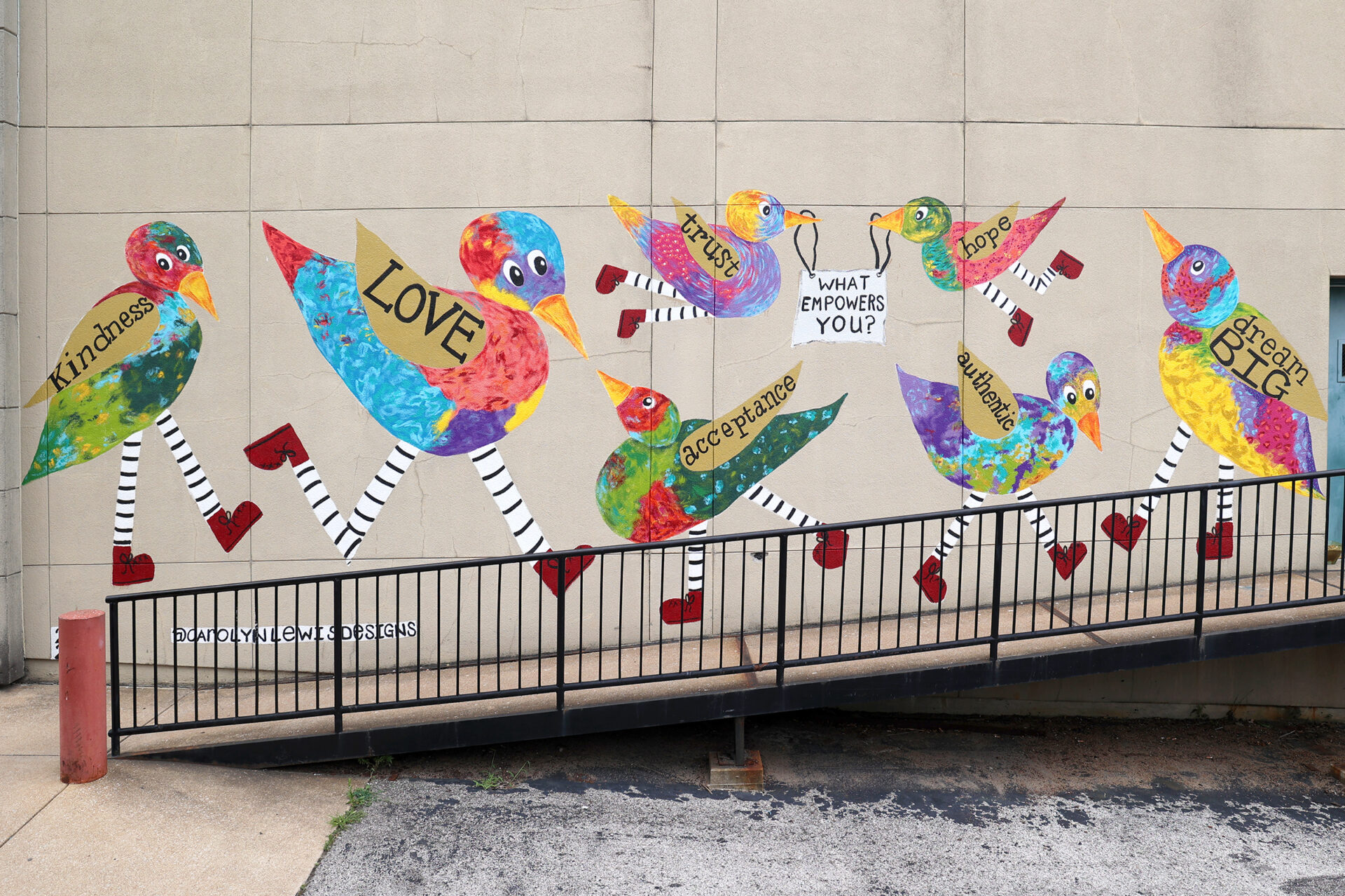 mural on the side of a building of colorful birds with different words on their wings holding a sign that says "what empowers you".