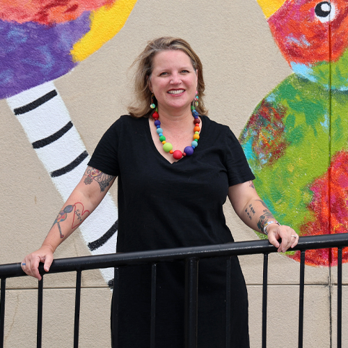 Carolyn Lewis in front of a painting of a rainbow